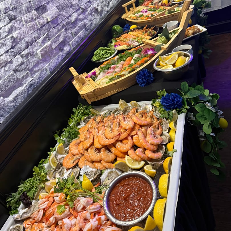 A seafood buffet with shrimp, oysters, and sushi boats, garnished with lemons and parsley.