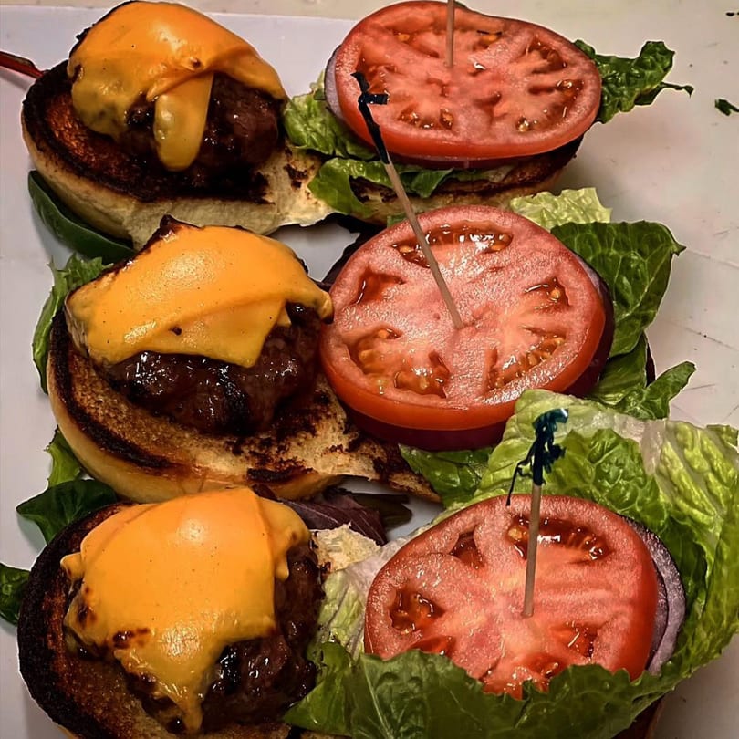 Three Nunzi's American Bistro cheeseburger sliders with lettuce, tomato, and onion on a white plate.
