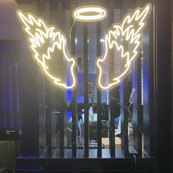 Neon angel wings and halo sign illuminate a dark room with blue lighting.