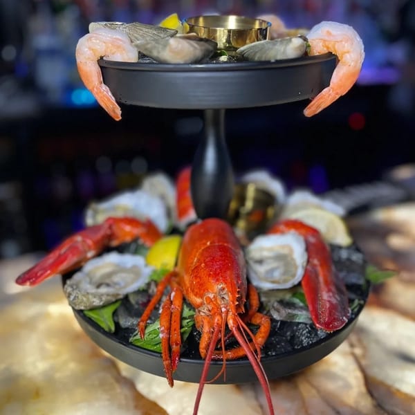 A two-tiered seafood tower with lobster, oysters, and shrimp on ice, garnished with lemon.