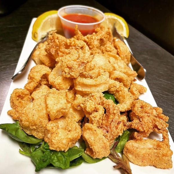 Crispy fried calamari with lemon wedges, marinara sauce, and fresh basil on a white plate.