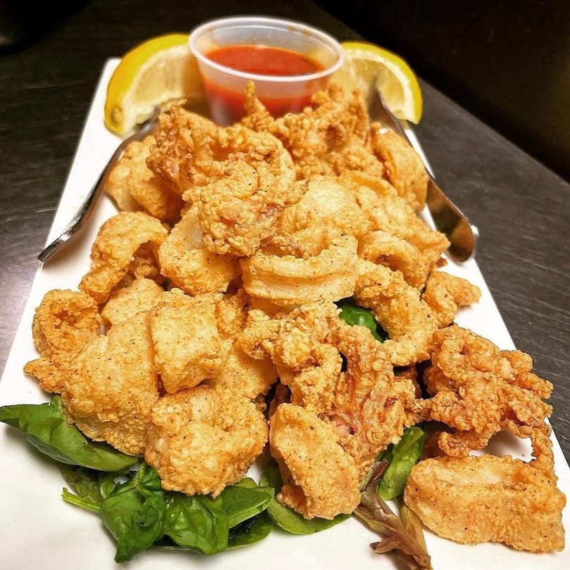 Crispy fried calamari with lemon wedges, marinara sauce, and fresh basil on a white plate.