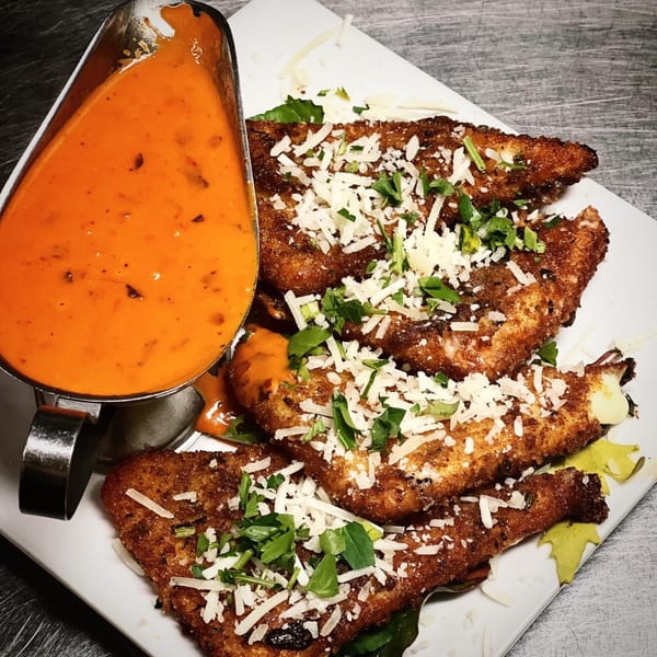 Crispy fried chicken cutlets topped with shredded cheese and herbs, served with a side of red sauce.