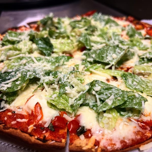 A close-up of a pizza topped with melted cheese, red sauce, and fresh green lettuce.